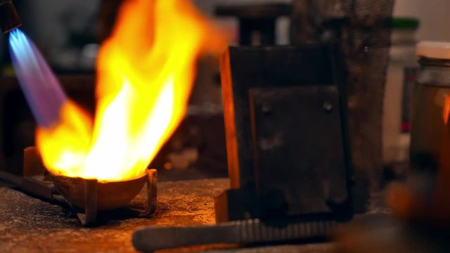 Goldsmith melting gold to liquid state in crucible with gasoline burner