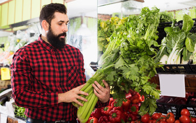 Positive man seller showing celery in shop