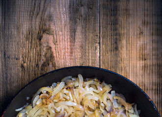 Fried onion in a frying pan. Blank space. View from above