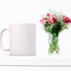 White blank coffee mug to add custom design/quote. Next to a vase of roses.