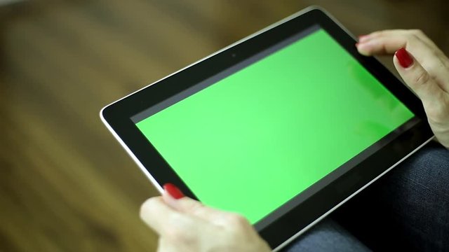 A woman holds a tablet computer with a green screen. Female fingers are holding the tablet. Tablet computer with a green screen for your content. 