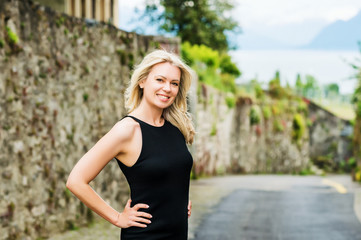 Outdoor portrait of young blond woman wearing black dress