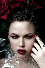 Fototapeta premium Beauty Fashion Model Woman face. Portrait with Red Rose flowers. Red Lips and Nails. Beautiful Brunette Woman with Luxury Makeup, perfect skin. Valentine.