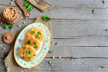 Fototapeta na wymiar Fried pea patties on a plate. Healthy diet patties cooked from yellow dried peas and decorated with parsley. Small barrel with dried peas on old wooden background with copy space. Vegetarian food