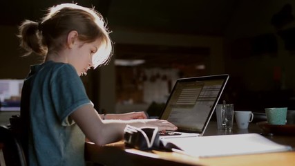 teenager girl doing homework on laptop with paperwork around her on desk