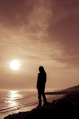 Obraz premium Silhouetted female figure stands on the coast at sunset