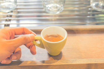 Hand holding yellow cup of coffee, Coffee espresso shot on woode
