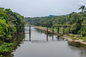 Fototapeta na wymiar Crumbling iron and concrete walking bridge crossing large river in rain forest of Cameroon, Africa
