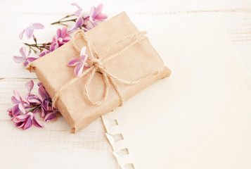 Handmade gift box in craft paper with twine, fresh spring lilac blossom, empty message background. Light soft dreamy colors. 
