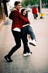 Two happy trendy teenage friends walking and dancing in the city, listening to the music with headphones, talking each other and smiling. Lifestyle, friendship and urban life concepts.