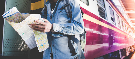 Obraz premium Młody mężczyzna trzyma mapę stojącą na peronie na stacji kolejowej do podróży. Koncepcja podróży pociągiem.