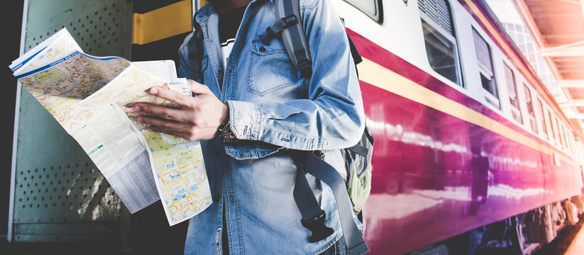 Fototapeta Young man holding map standing on platform at train station for travel. Travel concept by train.