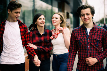 Four happy trendy teenage friends walking in the city, talking each other and smiling. Lifestyle, friendship and urban life concepts.