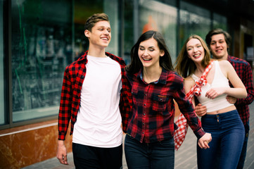 Four happy trendy teenage friends walking in the city, talking each other and smiling. Lifestyle, friendship and urban life concepts.