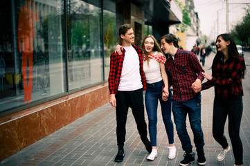 Naklejka premium Four happy trendy teenage friends walking in the city, talking each other and smiling. Lifestyle, friendship and urban life concepts.