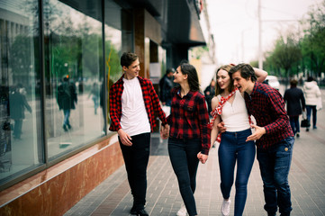 Four happy trendy teenage friends walking in the city, talking each other and smiling. Lifestyle, friendship and urban life concepts.