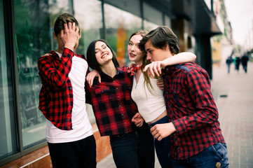 Four happy trendy teenage friends walking in the city, talking each other and smiling. Lifestyle, friendship and urban life concepts.