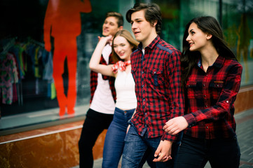 Obraz na płótnie Canvas Four happy trendy teenage friends walking in the city, talking each other and smiling. Lifestyle, friendship and urban life concepts.