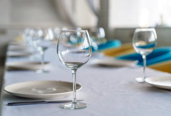 Set of clean empty wine glasses and plates on a dining table with colorful chairs on a restaurant interior pastel background. A close up view of cultery set for a meal