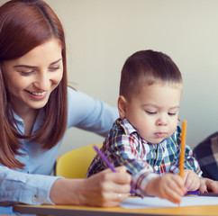 Portrait of happy pretty mother with her toddler son drawing