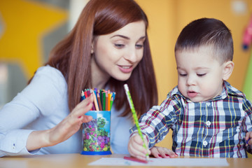 Portrait of happy pretty mother with her toddler son drawing