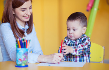 Portrait of happy pretty mother with her toddler son drawing