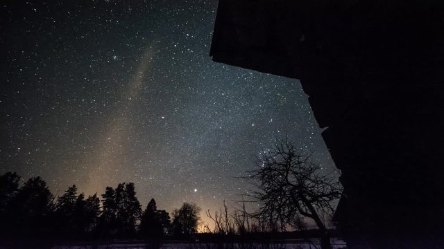 Timelapse of stars over timber house at winter night then clouds coming on dark sky.