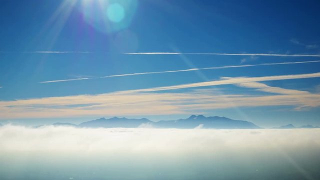 Majestic timelapse shot of fog covering landscape. Scenic view of vapor trails in sky on sunny day. Idyllic view of silhouette mountains are surrounded by rolling clouds. 4K resolution.
