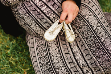 Schwangere Frau hält alte Kinderschuhe vor ihrem Bauch