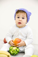 Cute little caucasian boy 11 months old sits and eats red apple on white background