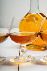 Glasses with cognac and a bottle on  white wooden background