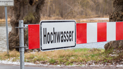 Road barrier with flood warning sign in front of flooded road in germany