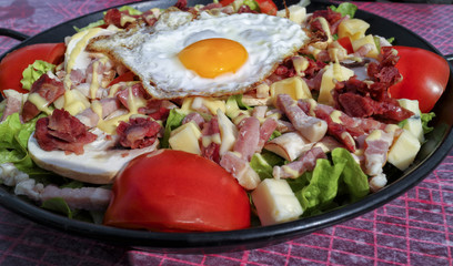 Plate of fried egg, chunks of bacon, sausage, cheese served with red tomato and lettuce