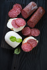 Bruschettas with salami and cheese over black wooden surface