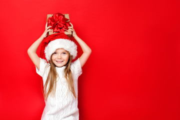 Happy girl in Christmas caps with gift wrapped in craft paper and red ribbons on red background. Christmas. Happy family.