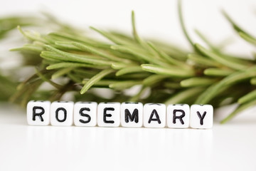 Blurred branch of rosemary in the background with close-up on plastic letter beads spelling “rosemary”