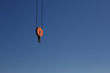 Orange crane hook against a clear blue sky