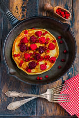 Homemade fried pancakes on a black cast iron skillet. Above are berries, raspberries, cranberries and blackberries. Wooden rustic brown background, vintage forks, top view.