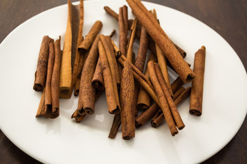 Cinnamon Sticks And White Plate On Wood Tabletop, From Side
