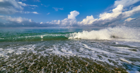 Tilt and shift view of green glowing sunny wave of Black Sea with frozen flying droplets under blue...