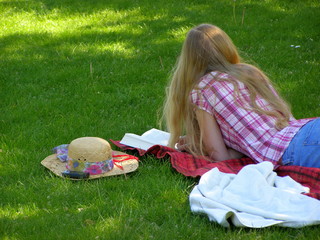 Kobieta czytająca książkę na trawie - obrazy, fototapety, plakaty