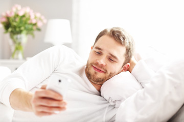 Handsome man lying in bed with smartphone