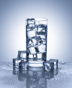 Glass of water with ice cubes on reflective surface