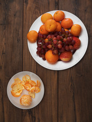 Clementines on a plate with grapes and apples  on a wooden table, top view.