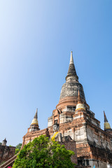 Fototapeta premium Buddha statue at the bottom of a large ancient pagoda on blue sky background at Wat Yai Chai Mongkon temple in Phra Nakhon Si Ayutthaya Historical Park, Ayutthaya Province, Thailand