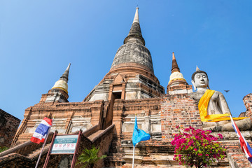 Buddha statue at the bottom of a large ancient pagoda on blue sky background at Wat Yai Chai Mongkon temple in Phra Nakhon Si Ayutthaya Historical Park, Ayutthaya Province, Thailand