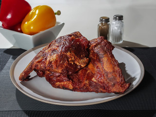 Smoked pork rib rack on a plate, With salt, pepper and plate with peppers in the background.
