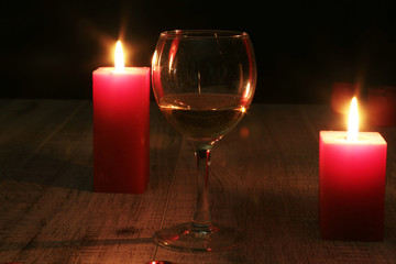 glass of wine or cognac and red candle on a wooden background.