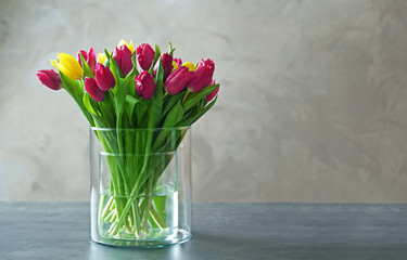 Glass vase with bouquet of beautiful tulips on color background