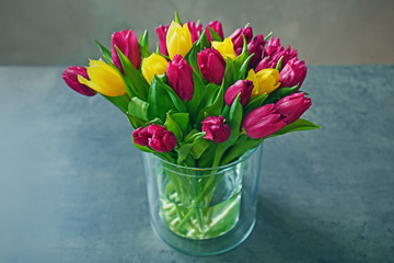 Glass vase with bouquet of beautiful tulips on color background